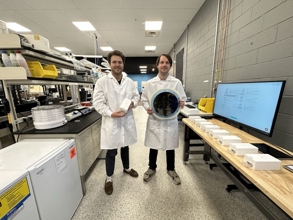 SiPhox Health co-founders standing in the SiPhox Health biochip pilot line and lab space. CEO Diedrik Vermeulen (right) is holding a 12" silicon photonics wafer with SiPhox's sensor chips and CPO Michael Dubrovsky (left) is holding the SiPhox Home device. (Photo: Business Wire)