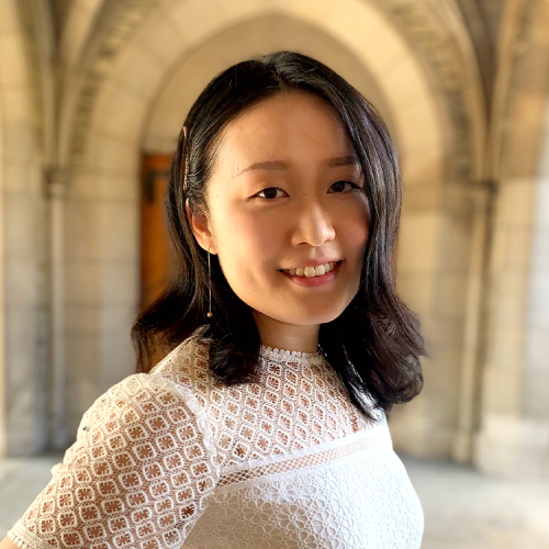 Yunxin stands smiling at the camera framed by an out-of-focus gothic arch on Duke campus.